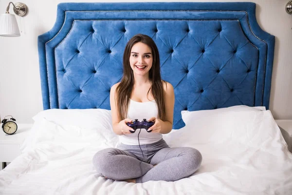 Joven mujer caucásica jugando videoconsola tumbada en la cama en casa —  Fotos de Stock