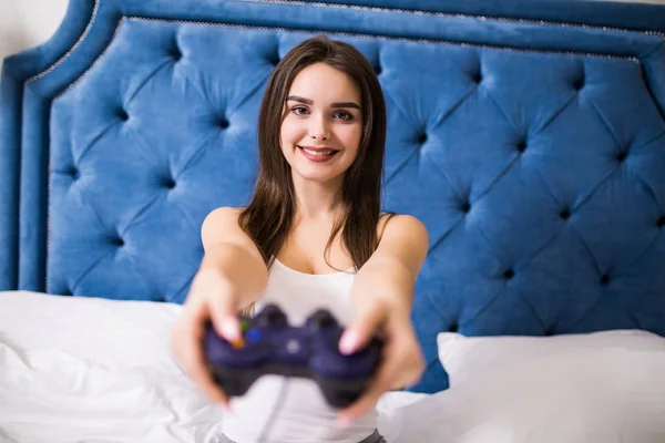 Jolie femme caucasienne brune en tenue de maison, s'asseoir au lit, jouer à des jeux vidéo avec tapis de jeu, regarder l'écran de télévision avec différentes émotions à la maison — Photo