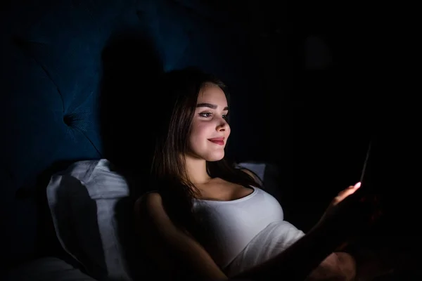 Young woman on bed late at night texting using mobile phone sleepy and tired in internet communication overuse concept and smart phone addiction — Stock Photo, Image