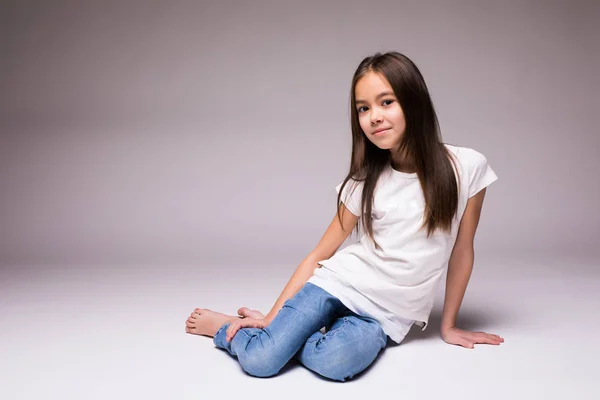 Adorable niña sonriente sentada en un suelo aislado sobre un fondo blanco — Foto de Stock