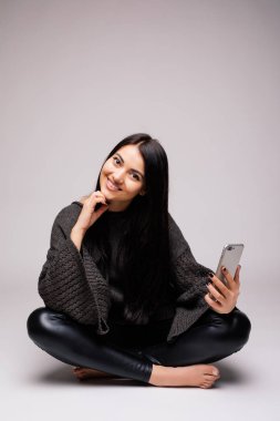 Gülümseyen katta oturan ve beyaz arka plan üzerinde smartphone kullanarak esmer kadın