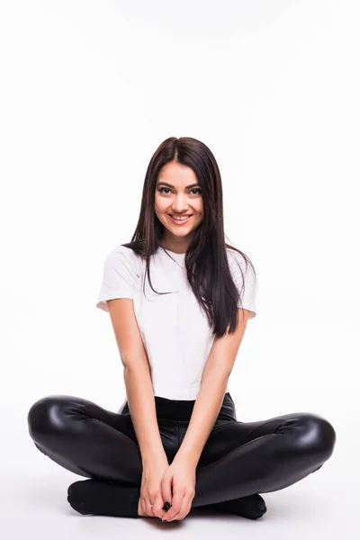 Молодая женщина сидит на полу и улыбается на белом фоне — стоковое фото