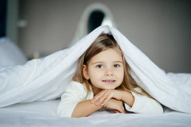 yatakta bir battaniyenin altında yalan ve evde gülümseyen kız