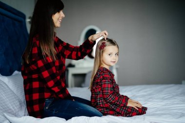 Güzel genç anne şirin küçük kızın saçını evde yatakta sabah araması yapıyor.