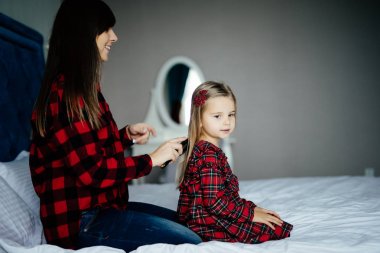 Güzel genç anne şirin küçük kızın saçını evde yatakta sabah araması yapıyor.