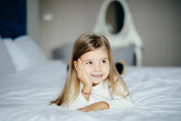 Söt leende liten flicka som vaknade i vit säng på morgonen — Stockfoto