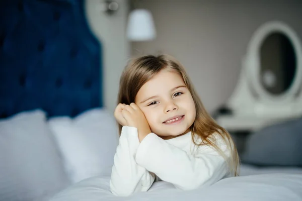 Close-up retrato de sorridente menina sentada com travesseiro branco na cama, olhando para a câmera — Fotografia de Stock