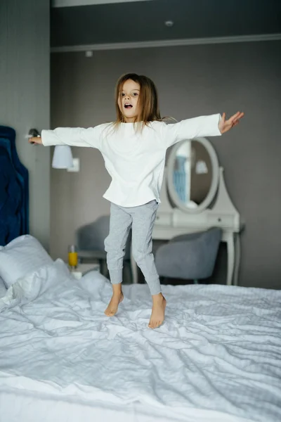 Симпатичная девочка прыгает и веселится на белой кровати — стоковое фото
