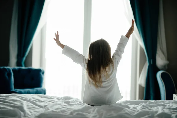 A nice child girl enjoys sunny morning in the bed. Good morning at home. Child girl wakes up from sleep.