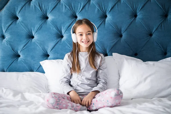 Primer plano de linda chica sonriente en los auriculares sentados en la cama, mirando a la cámara en casa — Foto de Stock