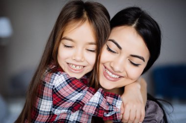 Güzel genç anne ve kızını sarılma ve yatağın evde kapalı gözler ile otururken gülümseyen