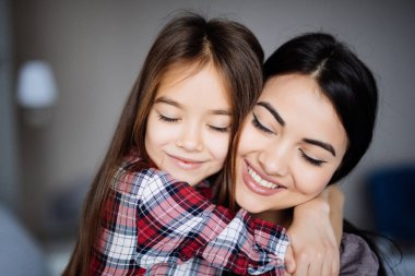 Güzel genç anne ve kızını sarılma ve yatağın evde kapalı gözler ile otururken gülümseyen