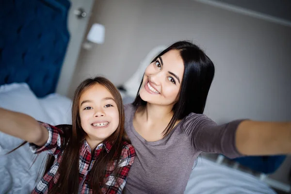 Young and older sisters making selfie in morning and have fun on bed in bedroom at home