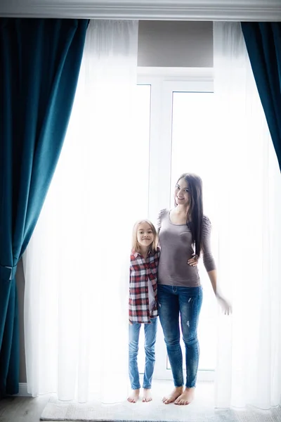 Молодая мать с дочерью открывают окна занавески в уютной спальне утром . — стоковое фото