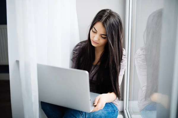 窓辺に座って、家でノート パソコンを使用しての美しい若い女性 — ストック写真