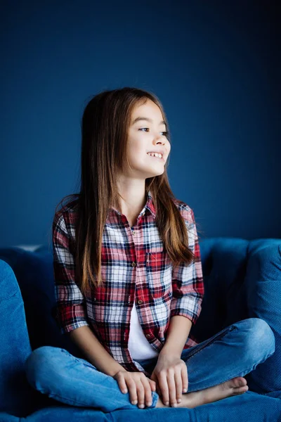 Pequeña niña sentada en la silla con sonrisa de belleza mira a la cámara en su habitación en casa — Foto de Stock