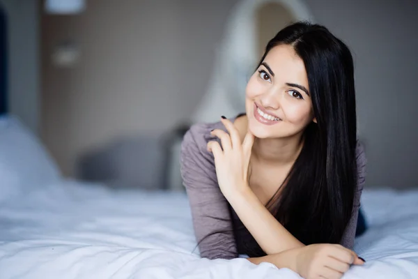 Fiatal nő keresi a kamera, és mosolyogva, miközben az ágyon otthon — Stock Fotó