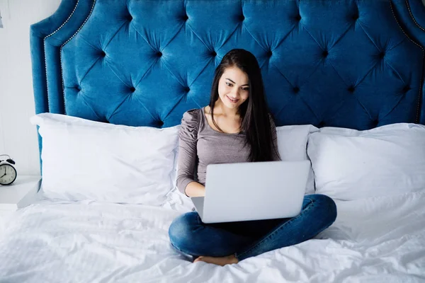 Retrato de una hermosa joven feliz tumbada en la cama y usando el ordenador portátil en casa — Foto de Stock