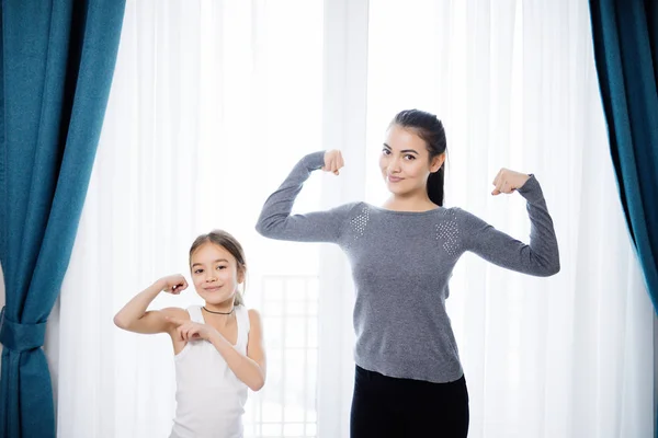 Young Mother and daughter showing strong hands while working out at home — Stock Photo, Image