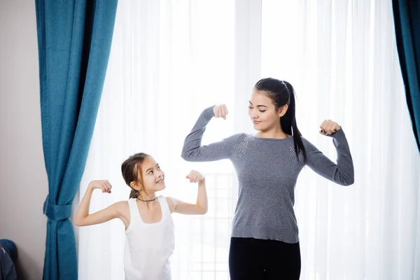 Молодые мать и дочь показывают сильные руки во время тренировки дома — стоковое фото