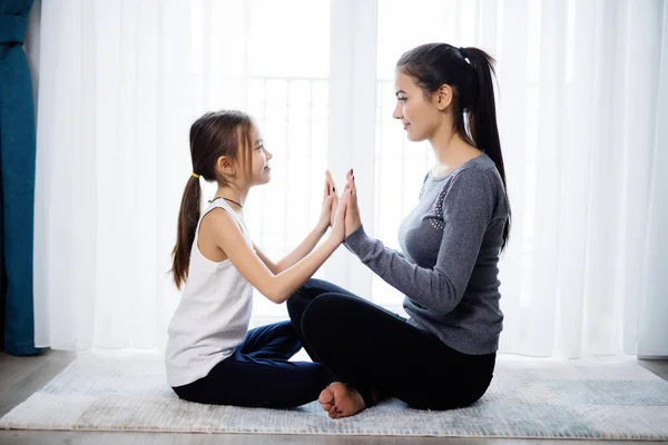 美丽的年轻女子和她迷人的小女儿在家里一起做瑜伽时，脸上挂着笑容 — 图库照片