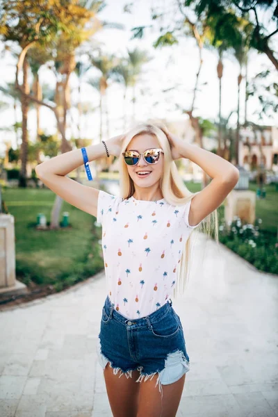 Ontspannen happy glimlach jonge vrouw in hoed en zonnebril op het terras van hotel op palmen achtergrond. Zomer roeping — Stockfoto