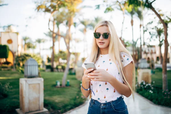 Lycklig ganska ung kvinna promenader och med smartphone på sommaren resort — Stockfoto