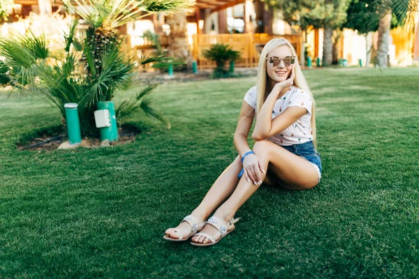 Szépség Szőke nő ül a fűben, a napszemüveg a nyári napokon. Nyári. — Stock Fotó