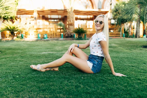 Mujer rubia belleza sentada en la hierba en gafas de sol en los días de verano. Verano . —  Fotos de Stock