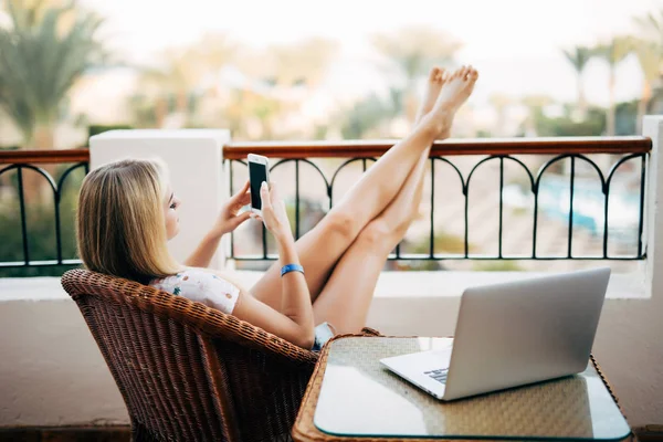 Telefon kullanarak ve rahatlatıcı ayak ile günün sonunda kadar balkonda kadın