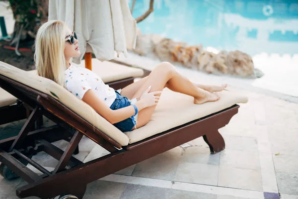 Fiatal szőke nő fürdőruhát a kanapé longue, hivatását nyáron a medence mellett pihentető — Stock Fotó