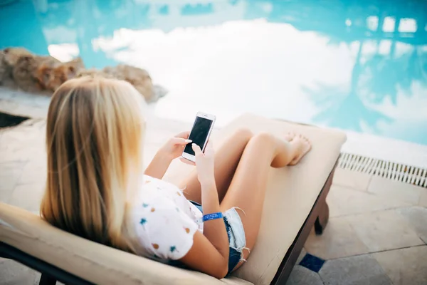 Женщина на шезлонге с телефоном на летнем отдыхе у бассейна — стоковое фото