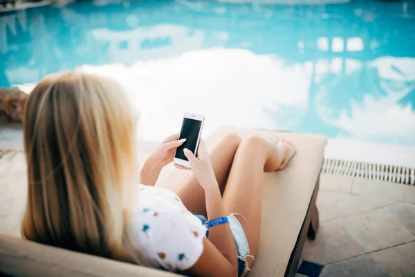 Молодая женщина в купальнике расслабляется в шезлонге и занимается серфингом в Интернете на телефоне для отправки смс . — стоковое фото