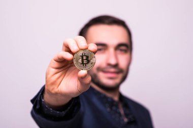 Genç yakışıklı adam altın bitcoin gri arka plan üzerinde izole kamera işaret etti