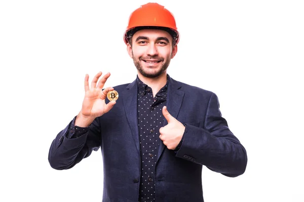 Joven minero guapo con hemlet protector sostiene Bitcoin en su mano y pulgares hacia arriba aislado en blanco. Concepto minería criptomoneda de Bitcoin — Foto de Stock