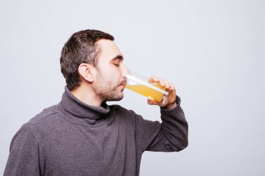 Yakışıklı adam gri arka plan üzerine portakal suyu içiyor