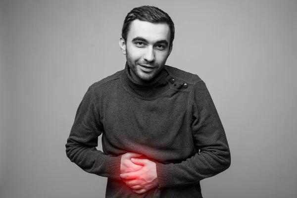 Genç adam onun hasta mide ağrı, gri arka plan, kırmızı sertleştirme için bir sembol olarak tek renkli fotoğraf izole holding — Stok fotoğraf