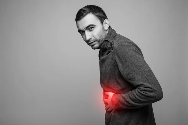 Junger Mann mit schmerzverzerrtem Bauch, isoliert auf grauem Hintergrund, monochromes Foto mit Rot als Symbol für die Verhärtung — Stockfoto