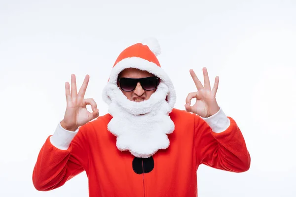 Ung man i santa claus pijama och solglasögon visar ett ok tecken på vit bakgrund — Stockfoto