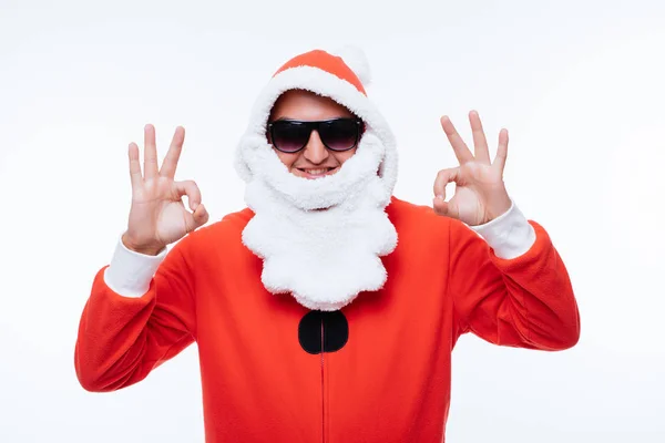 Ung man i santa claus pijama och solglasögon visar ett ok tecken på vit bakgrund — Stockfoto