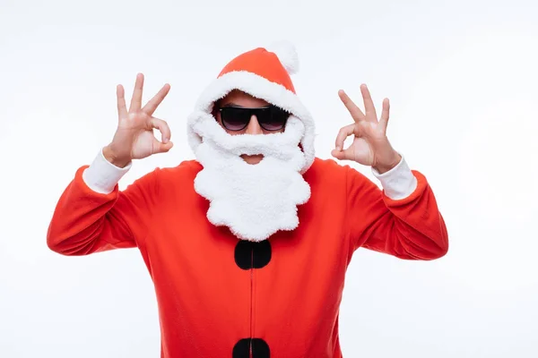 Genç adam Noel Baba pijama ve beyaz arka plan üzerinde ok işaretiyle gösterilen güneş gözlüğü — Stok fotoğraf