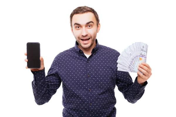 Portrét usměvavý veselý muž, který držel spoustu peněz bankovky při zobrazení prázdné obrazovky mobilního telefonu a při pohledu na fotoaparát izolované na bílém pozadí — Stock fotografie
