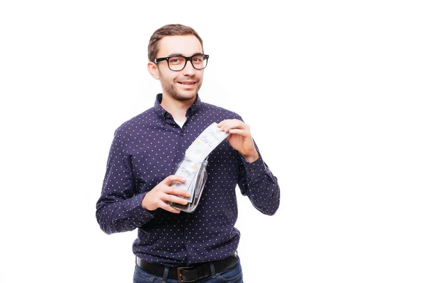 Retrato de homem confiante satisfeito em óculos colocar dólares frasco de notas de dinheiro isolado sobre branco — Fotografia de Stock