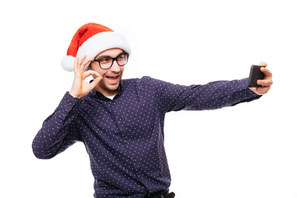 Gelukkig man in santa hat zwaaien en nemen selfie op smartphone, geïsoleerd op witte achtergrond — Stockfoto