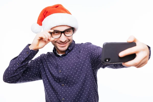 Νέοι ευτυχισμένος άνθρωπος συναισθηματική φορώντας Χριστουγέννων santa καπέλο στέκεται απομονωθεί σε λευκό τοίχο. — Φωτογραφία Αρχείου