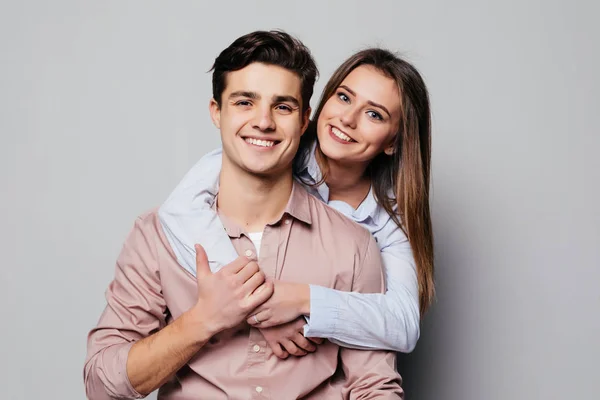Porträtt av ett glatt ungt par som kramas samtidigt står och tittar på kameran över grå — Stockfoto