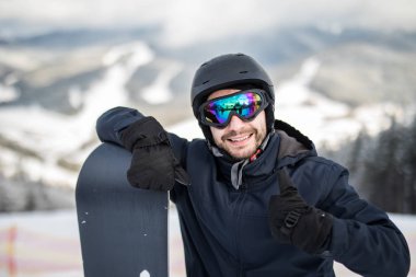 Kış Kayak Merkezi başparmak gösterilmesini kameraya gülümseyen adam snowboard snowboard ile karlı yamaç üstünde ayakta. Kayak ve snowboard kavramı