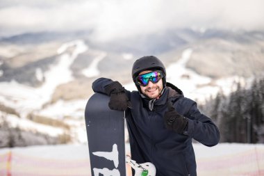 Kış Kayak Merkezi başparmak gösterilmesini kameraya gülümseyen adam snowboard snowboard ile karlı yamaç üstünde ayakta. Kayak ve snowboard kavramı