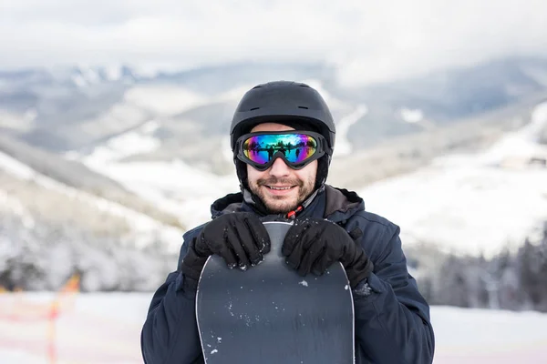 Snowboarder em terno de esqui e capacete com snowboard em montanhas — Fotografia de Stock