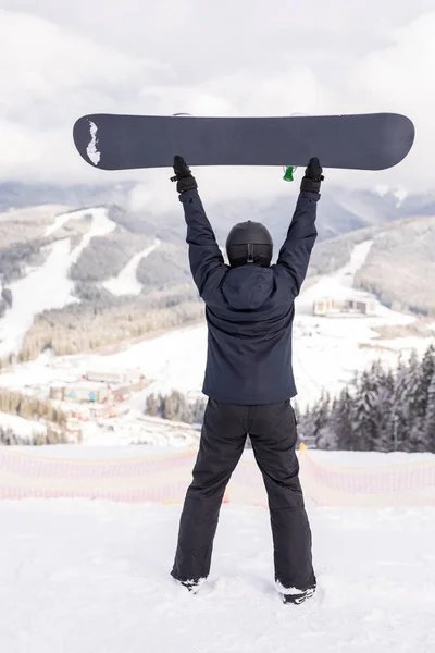 Hombre feliz de pie con snowboard sobre su cabeza en la cima de la colina de las montañas —  Fotos de Stock